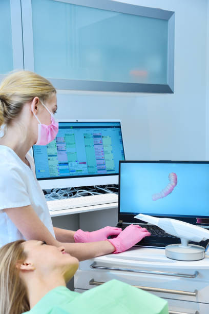 Woman dentist and patient looking at dental 3d scan on laptop screen stock photo