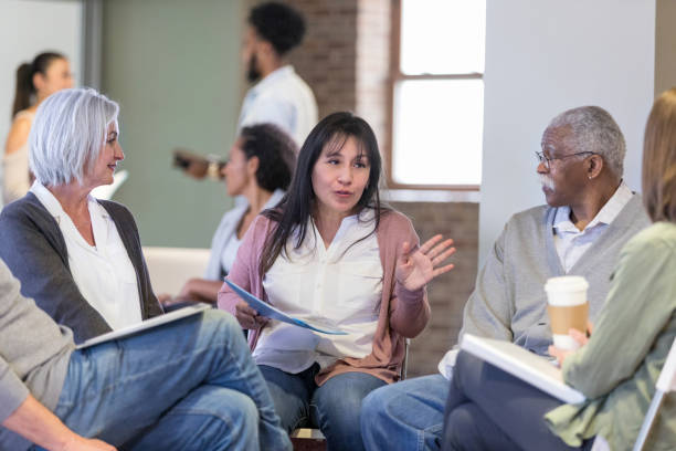 Woman discusses neighborhood issues during HOA meeting Mid adult Hispanic woman gestures as she discusses neighborhood concerns during a homeowner association meeting. group therapy stock pictures, royalty-free photos & images