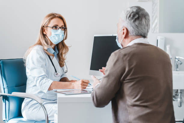 Woman doctor wear protection face mask talking with patient in clinic office Woman doctor wear protection face mask talking with patient in clinic office general practitioner stock pictures, royalty-free photos & images