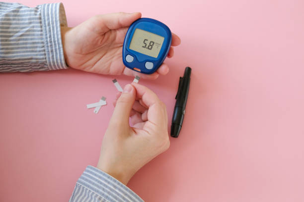 Woman doing blood glucose measurement using glucometer. Gestational diabetes mellitus concept. Female hands holding glucometer with test strip, lancelet on pink background. hyperglycemia stock pictures, royalty-free photos & images