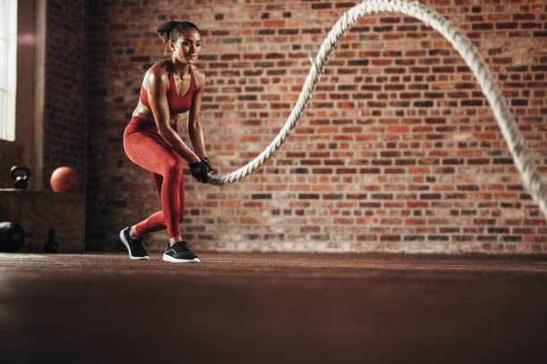 Woman doing cross training routine Woman using training rope for exercise at gym. Athlete working out with battle rope at cross training gym. cross training stock pictures, royalty-free photos & images