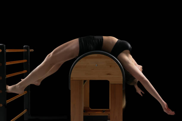 Woman doing pilates exercises in a barrel equipment, black backgound, low key. stock photo