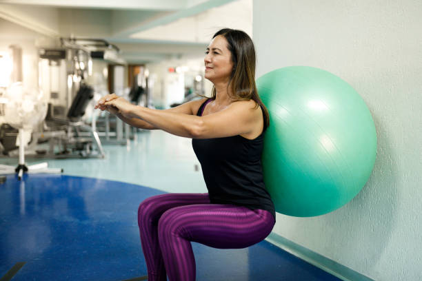 Woman doing squatting with exercise ball Seniors at gym woman with ball doing squats stock pictures, royalty-free photos & images