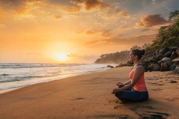 Woman doing yoga at beach - Padmasana lotus pose Woman doing yoga - meditate and relax in Padmasana Lotus asana pose with chin mudra outdoors at tropical beach on sunset with dramatic sun self-care stock pictures, royalty-free photos & images