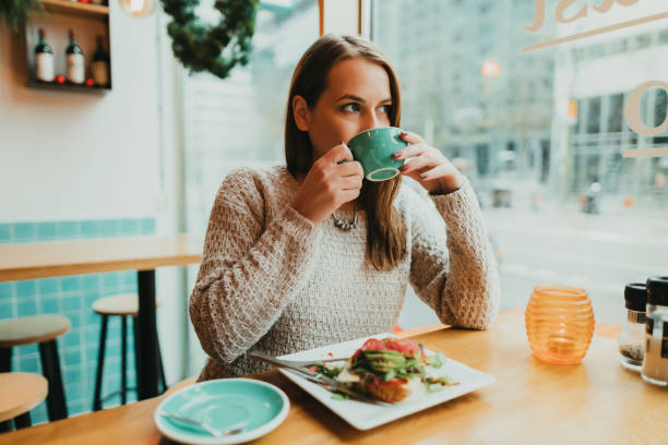 Woman drinking coffee and eating avocado toast in the restaurant stock photo
