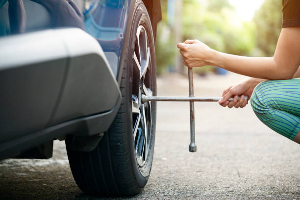 Woman driver with tyre iron changing wheel on a roadside stock photo