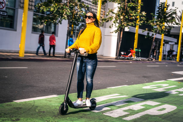 una donna alla guida di uno scooter elettrico su uno scooter e una pista ciclabile nel centro della città - electric scooter foto e immagini stock
