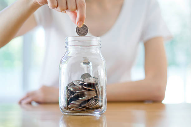 Woman Dropping Coins Into Glass Jar stock photo