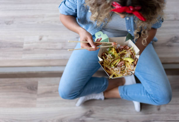 Woman eating a poke bowl at home while moving house Close-up on a woman eating a poke bowl at home while moving house take out food stock pictures, royalty-free photos & images