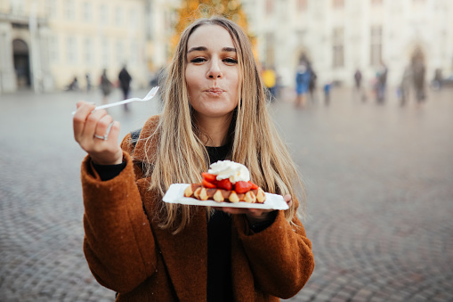 Woman in cafe eating belgium waffles with chocolate sauce, ice cream and strawberries.
