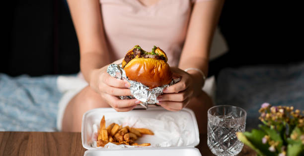 femme mangeant le hamburger et les frites livrées à la maison seule - eating burger photos et images de collection