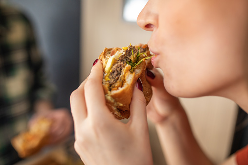 Young woman eating delicious burger in fast food restaurant