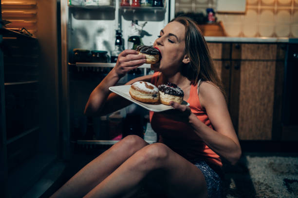 Woman eating doughnuts in front of the refrigerator stock photo