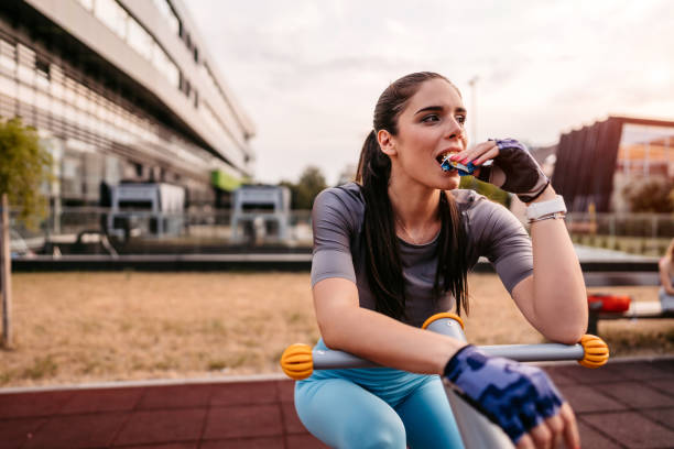 Woman eating energy bar after riding bike in park stock photo