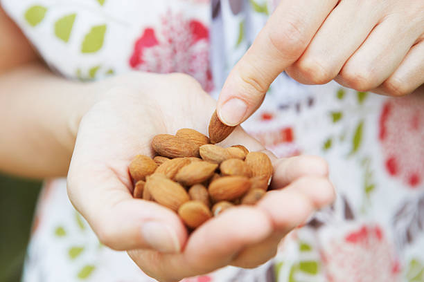woman eating handful of almonds - amandel noot stockfoto's en -beelden