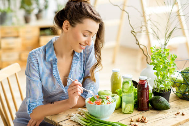 Woman eating healthy salad Young and happy woman eating healthy salad sitting on the table with green fresh ingredients indoors eating stock pictures, royalty-free photos & images
