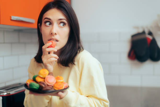 Woman Eating Macarons Feeling Guilty and Hiding stock photo