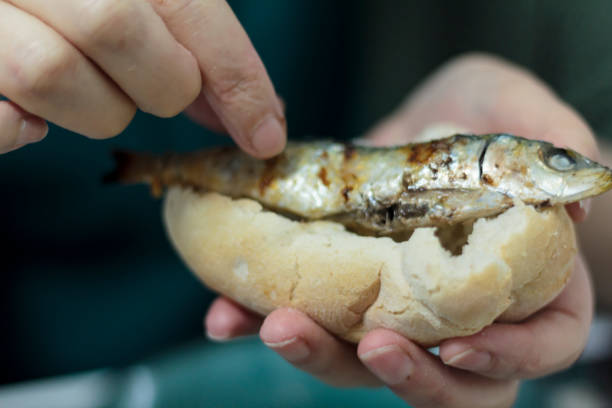 Woman eating roasted sardines with her hands stock photo