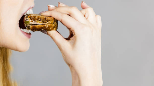 Woman eating sandwich, taking bite Young woman eating sandwich, taking bite with wide open mouth. Food, calories, dieting concept. Studio shot on grey background, profile view. chewing stock pictures, royalty-free photos & images