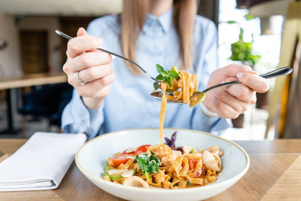 Woman eats Italian pasta with seafood and tomato sauce. I'm Pasta Gamberini. Close-up tagliatelle wind it around a fork with a spoon. Parmesan cheese stock photo