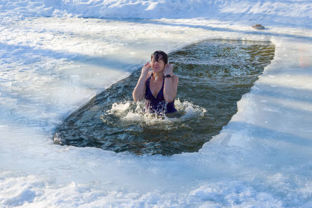 een vrouw blijkt uit het ijsgat. dag van de doop - ice swimming stockfoto's en -beelden