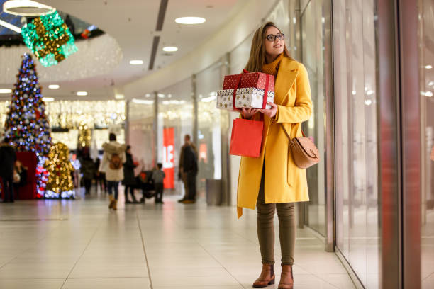 woman enjoying christmas shopping at the mall - woman holding a christmas gift imagens e fotografias de stock