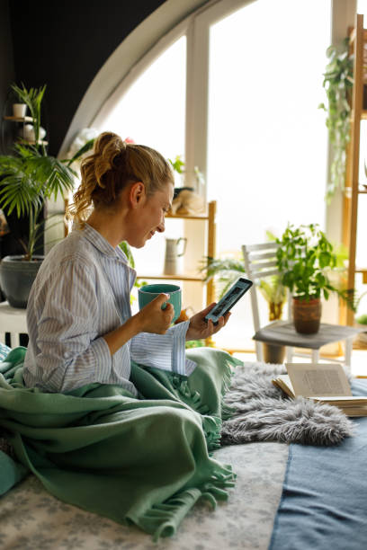Woman enjoying coffee in bed and reading news on smart phone stock photo