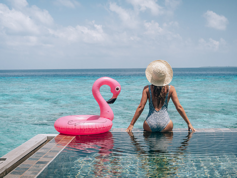 Woman enjoying tropical vacations from the edge of an infinity pool in private over water villa. People travel luxury holidays