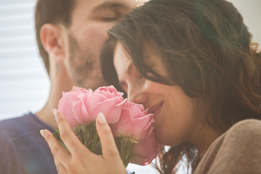Mid adult man and woman with bouquet of pink roses sharing romantic moments.