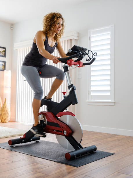 Woman Exercising on Spin Bike in Home A woman exercising on a spin bike using an online instructor inside a home. peloton stock pictures, royalty-free photos & images