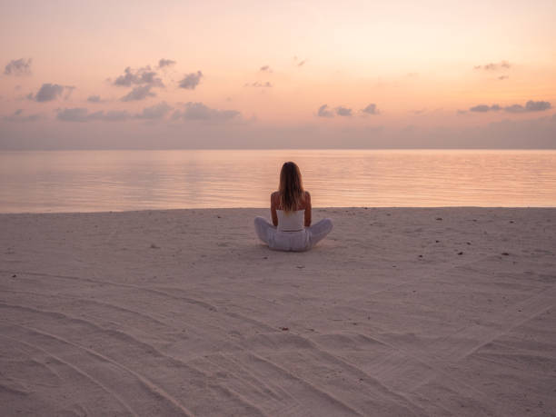 Woman exercising yoga at sunrise on the beach stock photo