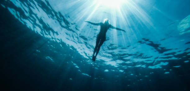 Woman floating in the sea and rays of light piercing through Underwater photo of woman floating in the sea and rays of light piercing through floating on water photos stock pictures, royalty-free photos & images