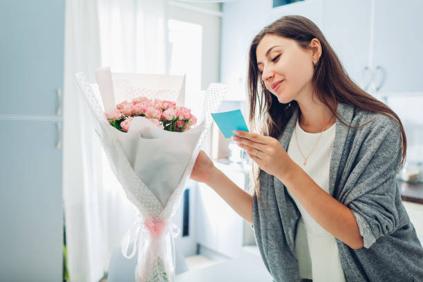 Woman found bouquet of flowers on kitchen and reading card on kitchen. Surprise. Present for holiday stock photo