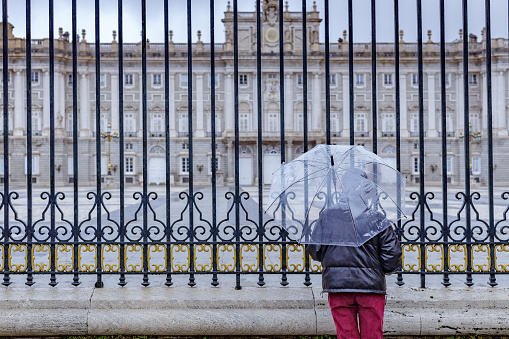 Madrid, Spain December 25 2021. Woman from behind looking at Royal palace facade on rainy day