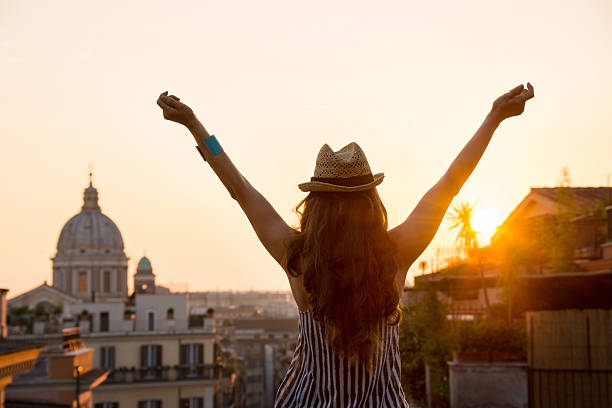 Woman from behind with outstretched arms in Rome at sunset Seen from behind, a woman is standing with outstretched arms, looking out at the city of Rome at sunset in summer. city break stock pictures, royalty-free photos & images