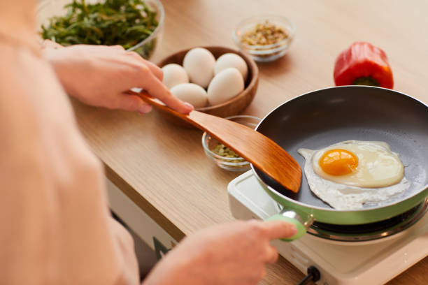 Woman Frying Eggs for Breakfast Warm-toned close up of unrecognizable young woman cooking eggs on frying pan while preparing healthy breakfast in morning, copy space fried egg photos stock pictures, royalty-free photos & images