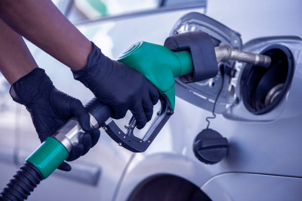 A woman fuelling gasoline at a gas station during coronavirus. Woman's hands inserting the nozzle into the vehicle tank, refueling gasoline during coronavirus, wearing black disposable nitrile gloves for virus protection. contamination photos stock pictures, royalty-free photos & images
