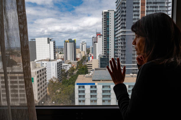 Woman gazing out window while in hotel quarantine during COVID pandemic stock photo