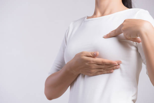 Woman hand checking lumps on her breast for signs of breast cancer on gray background. Healthcare concept. stock photo