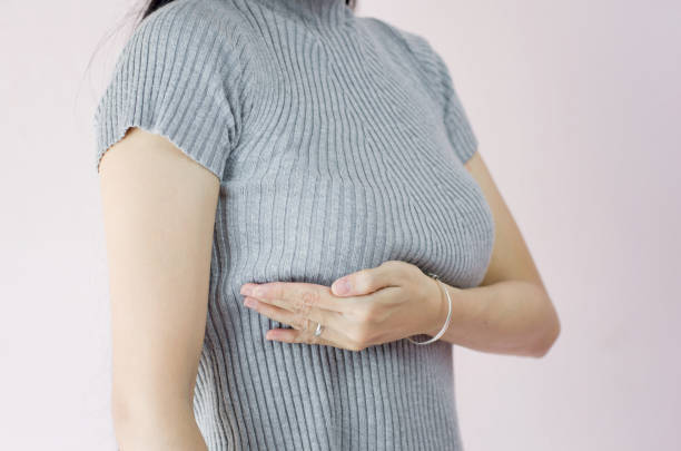 woman hand checking lumps on her breast for signs of breast cancer on crepe pink background, healthy lifestyle concept - beleza doentes cancro imagens e fotografias de stock