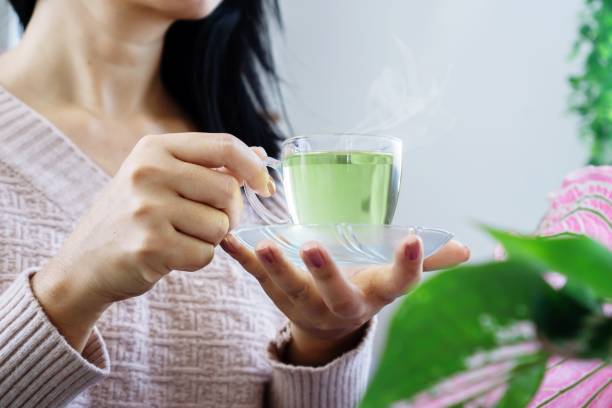 wanita tangan minum kaca teh hijau panas di pagi hari, konsep gaya hidup makan sehat - teh hijau potret stok, foto, & gambar bebas royalti
