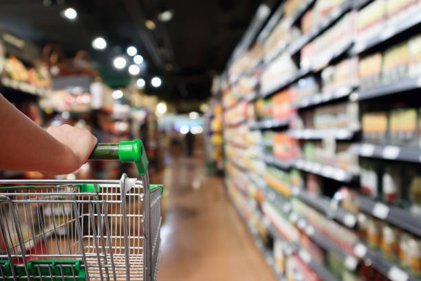 donna mano tenere carrello della spesa con abstract sfocatura supermercato corridoio sfondo - supermarket foto e immagini stock