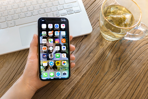 Seoul, May 5, 2020: Woman hand on the cafe table holding the home screen IOS 13 and iPhone 11. The iPhone was developed by Apple Inc.