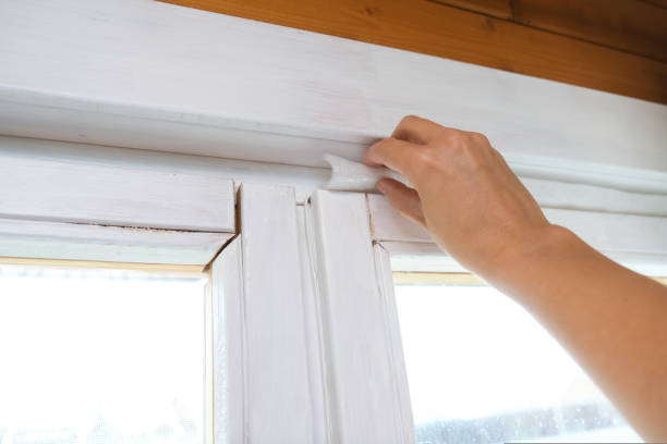 Woman hand insulating old windows to prevent warmth heat leak and drafts, preparing house for winter and cold weather stock photo
