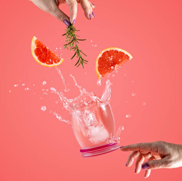 Woman hand support fly glass of grapefruit drink with splash, juice grapefruit slices falling in glass. Cocktail of grapefruit, thyme and rosemary flavor stock photo