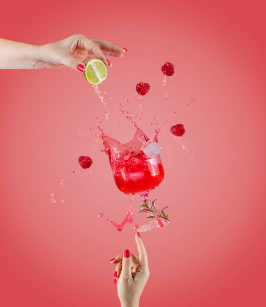 Woman hand support fly glass of raspberry drink with splash, juice raspberry falling in glass. Cocktail of raspberry, lime and rosemary flavor stock photo