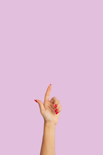 woman hand with red nail polish pointing up isolated on pink. space for text