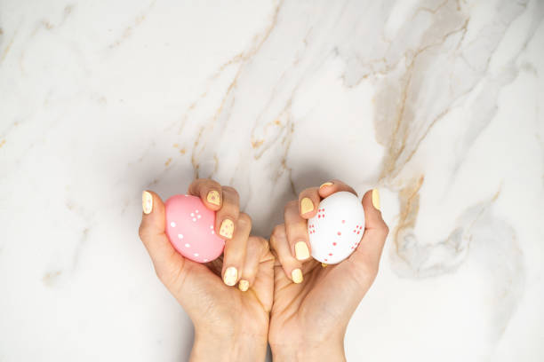 Woman hand with yellow manicure holding Easter eggs on marble background. stock photo