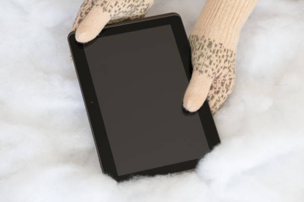 Woman hands in light teal knitted mittens are holding modern tablet...