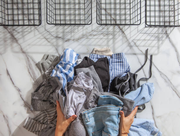 Woman hands putting stack of clean clothes for neatly tidying up and placing in steel wire wardrobe Woman hands putting stack of clean clothes for neatly tidying up and placing in steel wire wardrobe baskets organiser on the white marble table. modern style and space saving storage concept. marie kondo stock pictures, royalty-free photos & images